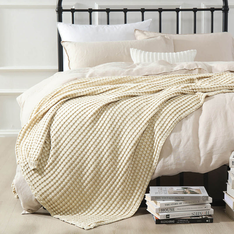 Temperature-regulating Cozy Bamboo Waffle Weave Throw Blanket in creamy neutral beige color used for layering on bed over duvet covers for a soft and cozy space relaxing and sleeping. Suitable for use on beds, couches and sofas for year-round comfort.