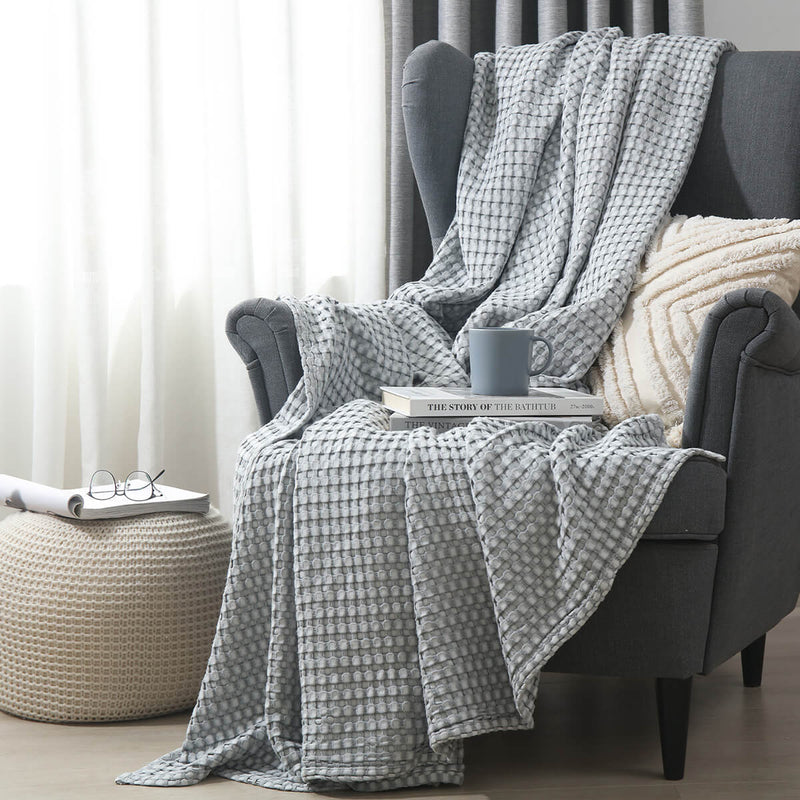 Temperature-regulating Cozy Bamboo Waffle Weave Throw Blanket in modern gray color on armchair for a soft and cozy space for sitting, napping, or relaxing. Suitable for use on beds, couches and sofas for year-round comfort.