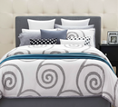 Bed with spiral patterned comforter and various pillows against a neutral wall.